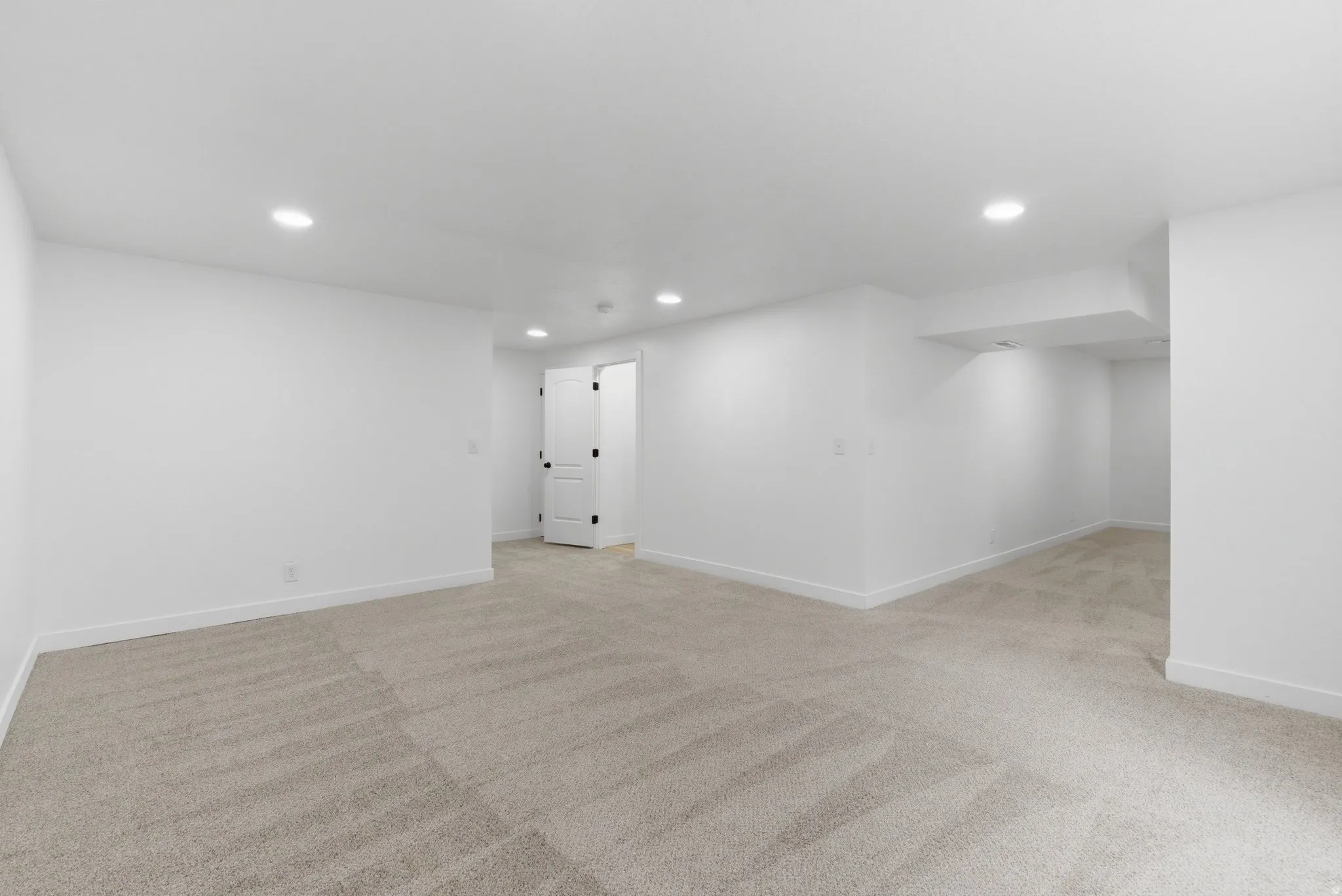 Spacious room featuring new carpeting, recessed lighting, white baseboards, and a white interior door with black hardware