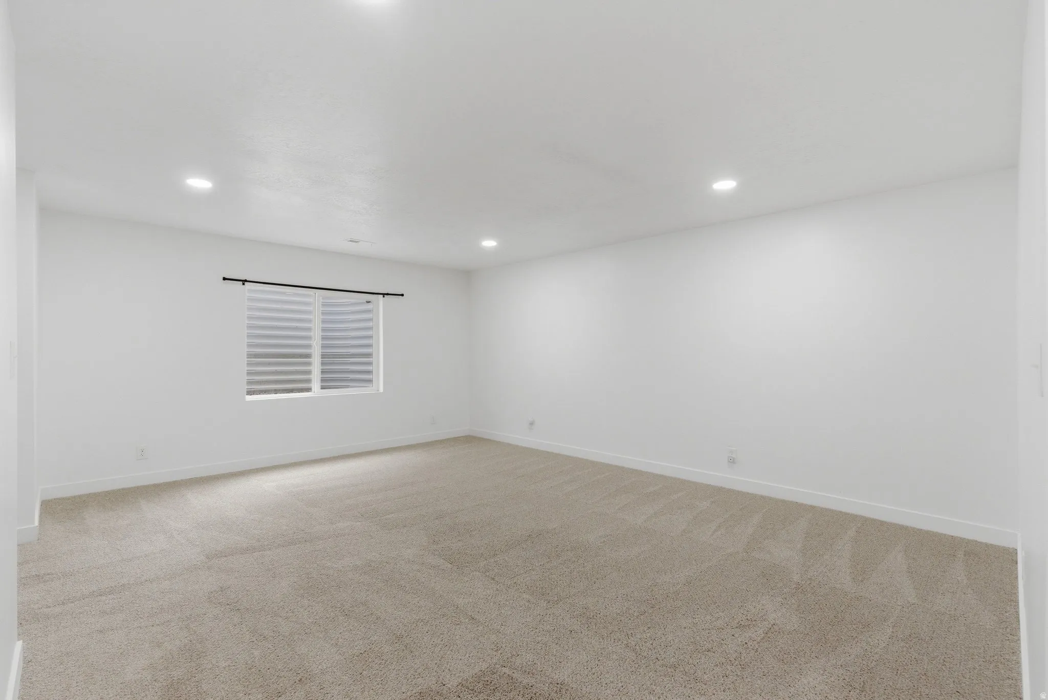 Spacious room featuring neutral carpeting, recessed lighting, a horizontal window with blinds, and white painted walls