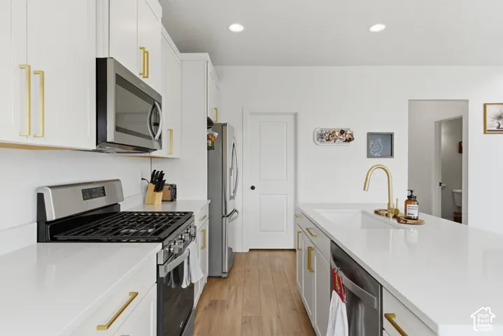 Modern kitchen featuring white cabinetry with gold-tone hardware, stainless steel appliances, light-toned countertops, a gas range, and wood-finish flooring