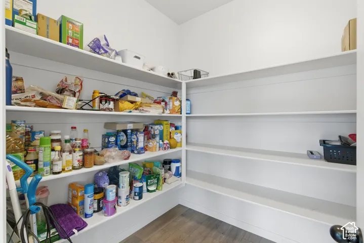 Corner pantry featuring multiple white built-in shelves, wood-finish flooring, and white walls
