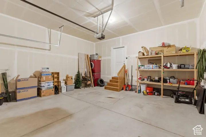 Spacious garage featuring a concrete floor, exposed ceiling joists, and a white interior door with wooden stairs