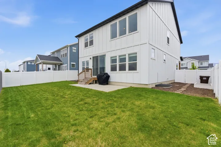 Spacious backyard featuring a large green lawn, a white privacy fence, and a concrete patio