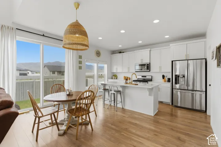 Open-concept kitchen and dining area featuring wood-finish flooring, white cabinetry, and stainless steel appliances