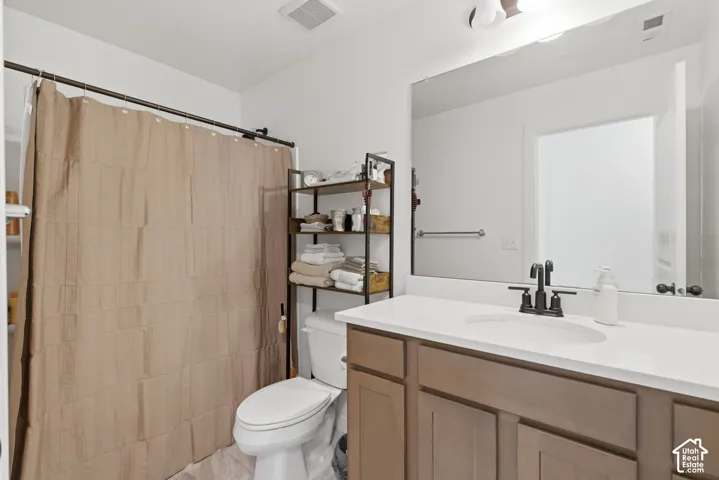 Bathroom featuring a single vanity with a white countertop and brown cabinetry, a large mirror, and a shower area with a curtain rod