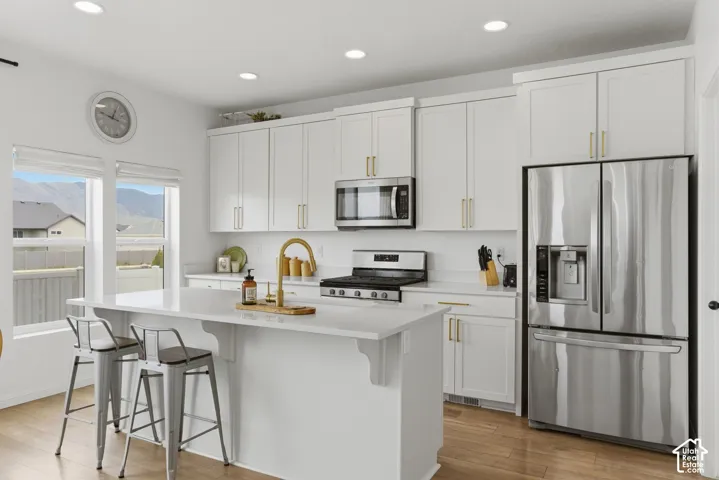 Modern kitchen featuring white shaker cabinetry with gold-finish hardware, stainless steel appliances, and a central island with a sink and seating