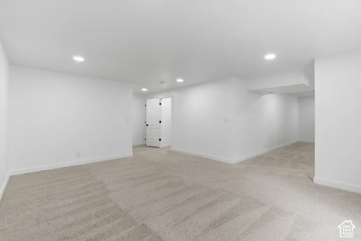 Spacious room featuring new carpeting, recessed lighting, white baseboards, and a white interior door with black hardware
