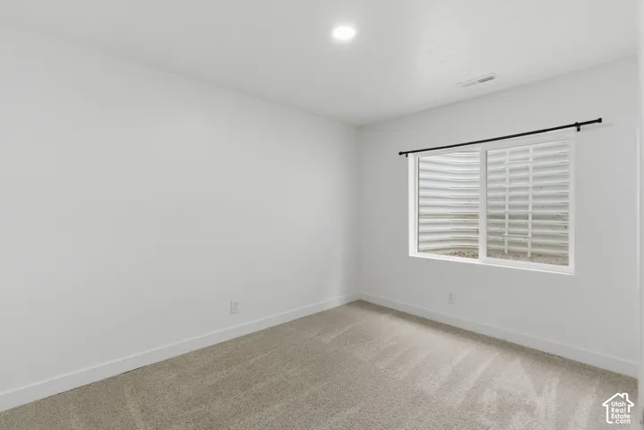 Carpeted room featuring a window with a window well, white walls, and recessed lighting