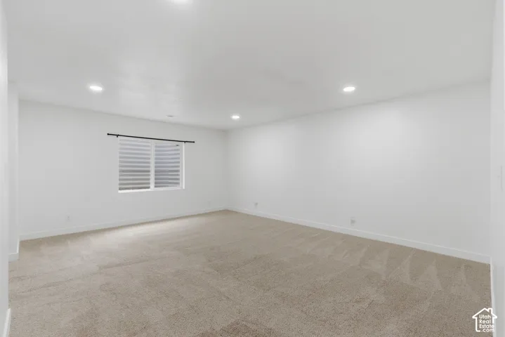 Spacious room featuring neutral carpeting, recessed lighting, a horizontal window with blinds, and white painted walls