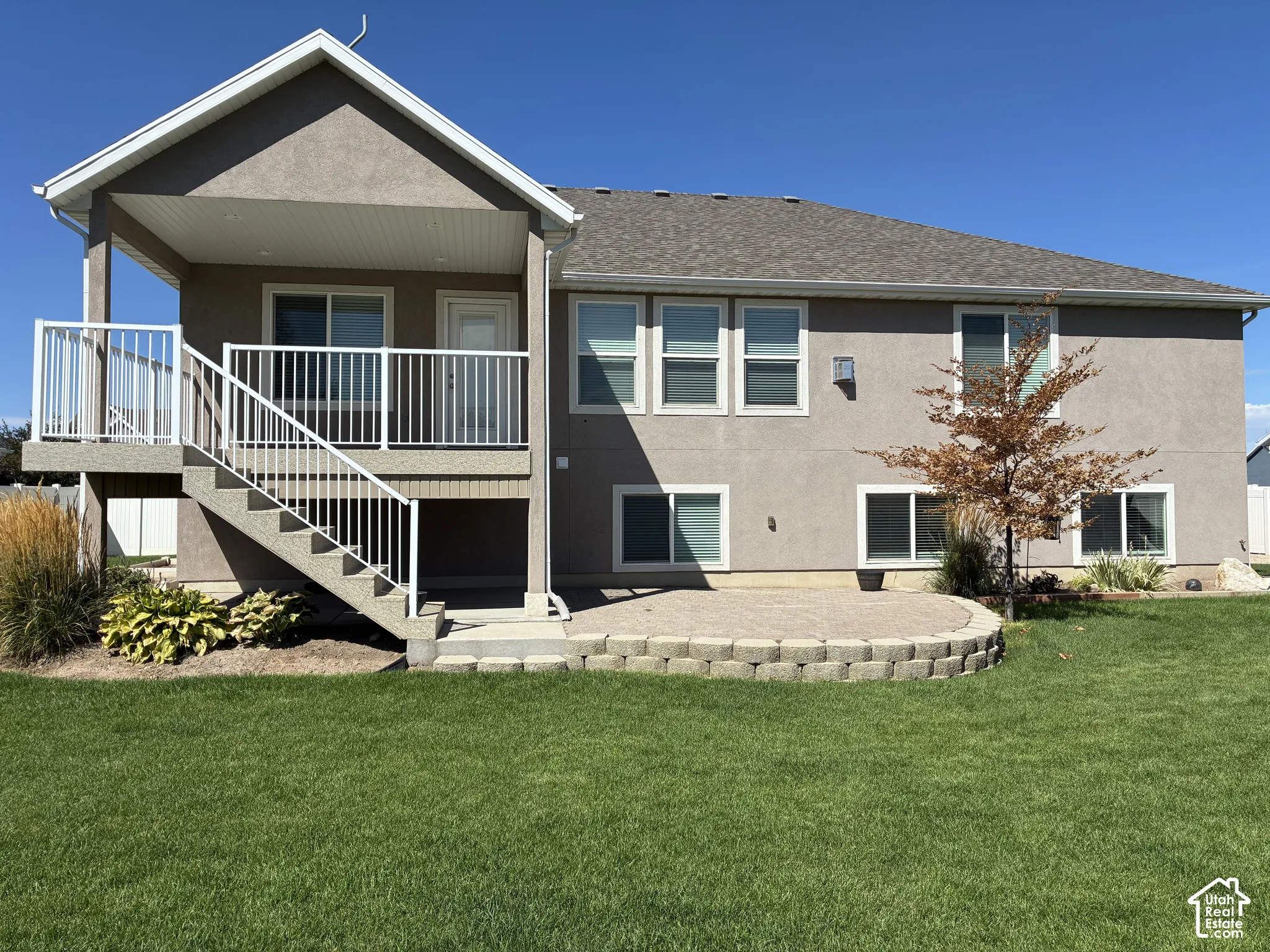 Expansive rear yard featuring a covered balcony, stone-paver patio, and stucco exterior
