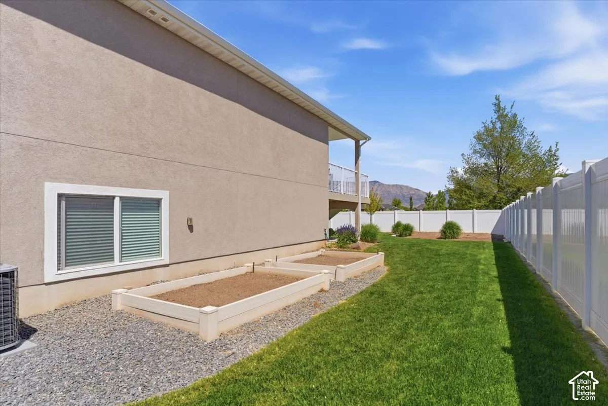 Expansive backyard featuring a manicured lawn, two raised garden beds, and a white privacy fence