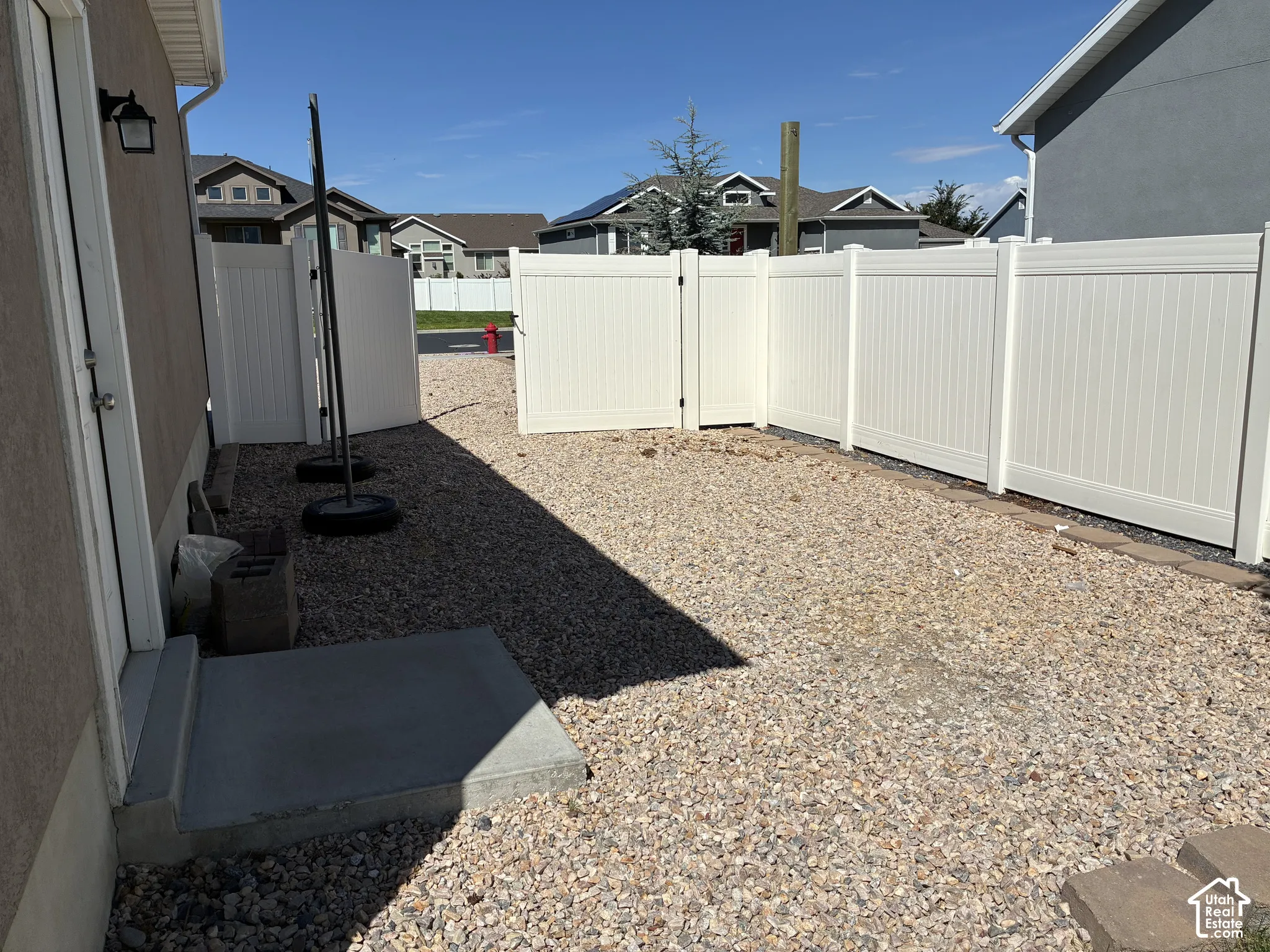 Gravel side yard with a white vinyl fence featuring a gate