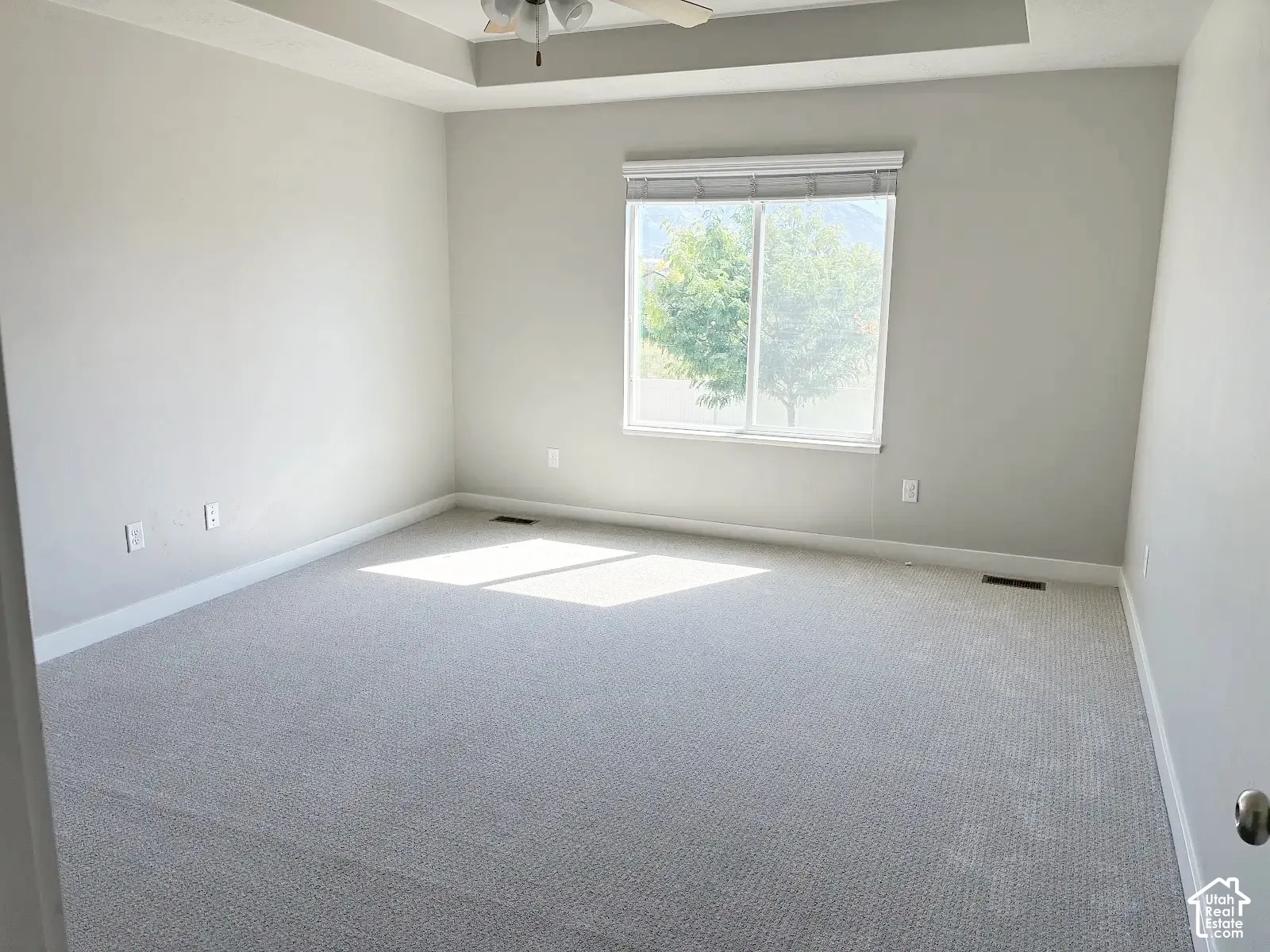Recessed tray ceiling with a ceiling fan, light gray wall paint, white trim, and a large window