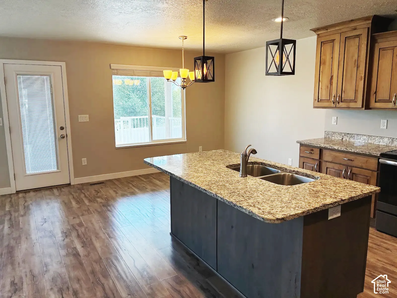 Kitchen featuring a center island with a double basin sink, granite countertops, wood-finish flooring, and pendant lighting
