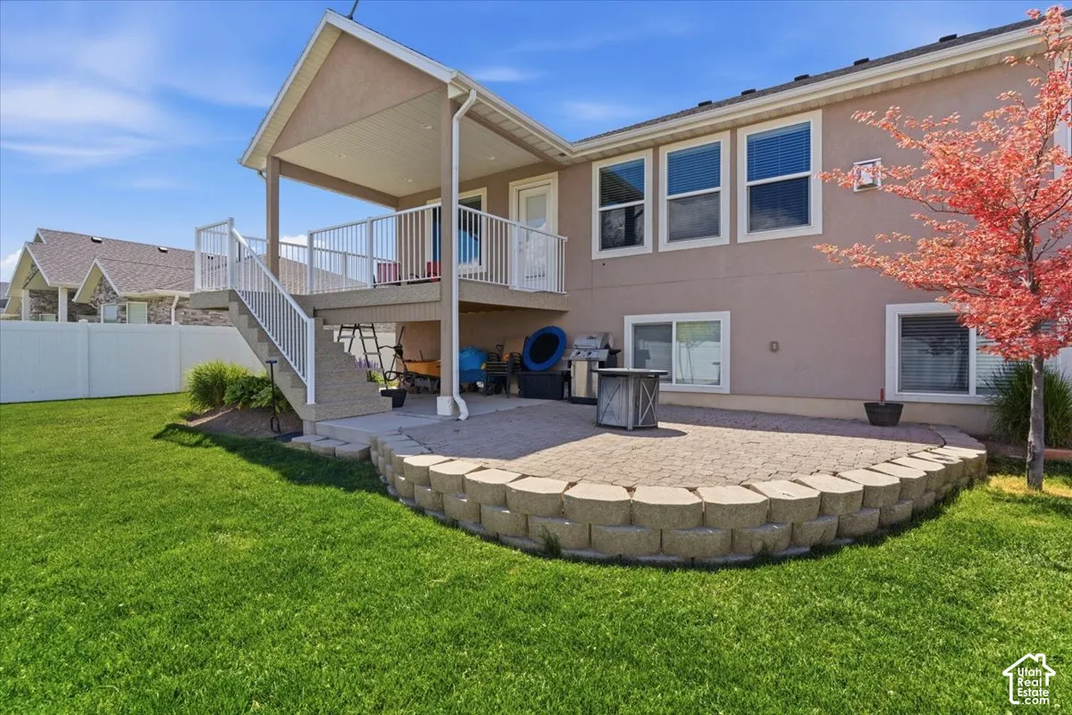 Expansive backyard featuring a manicured lawn, a large paver patio with a low retaining wall, and a covered upper deck with white railing
