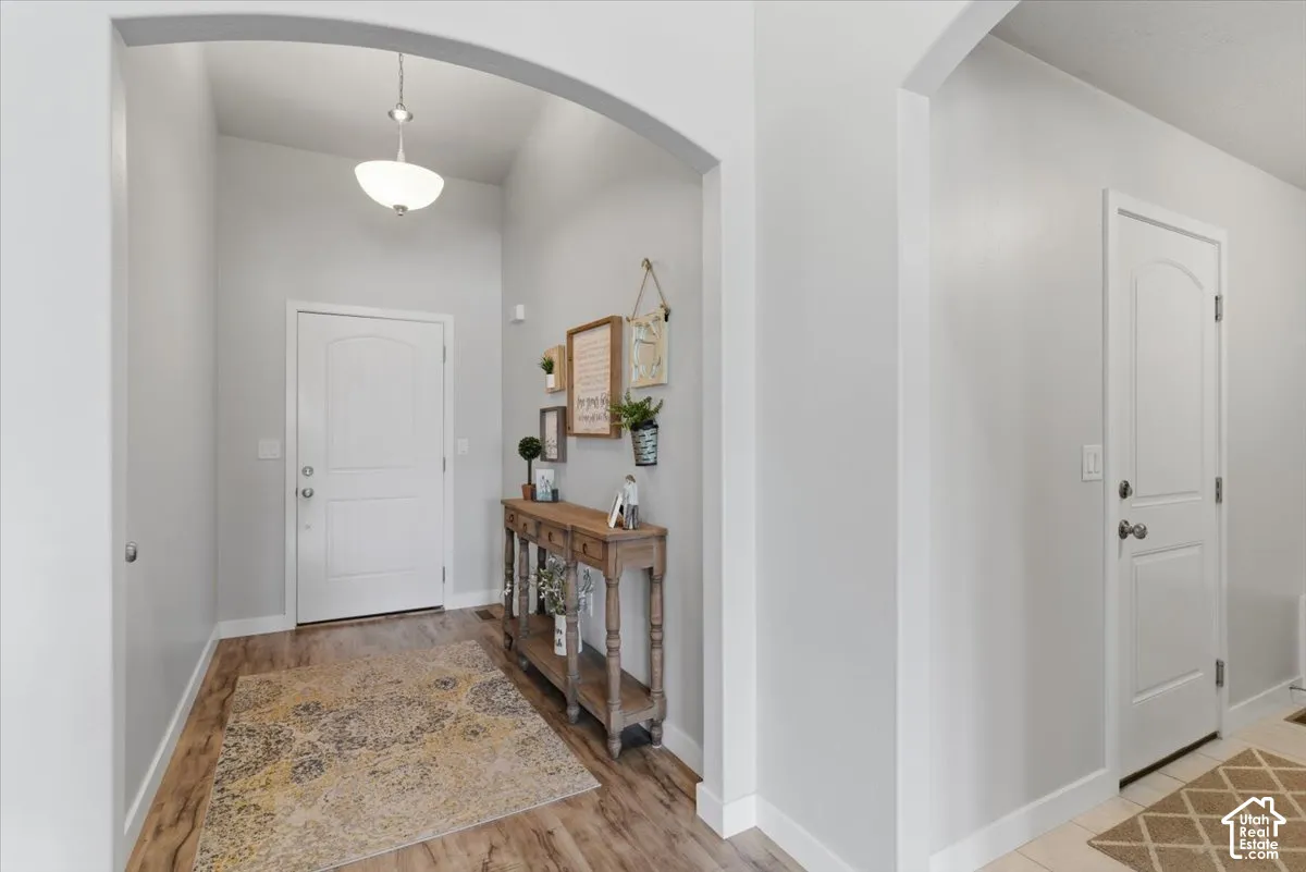 Entryway featuring an arched doorway, wood-finish flooring, a white paneled door, and a semi-flush mount ceiling light