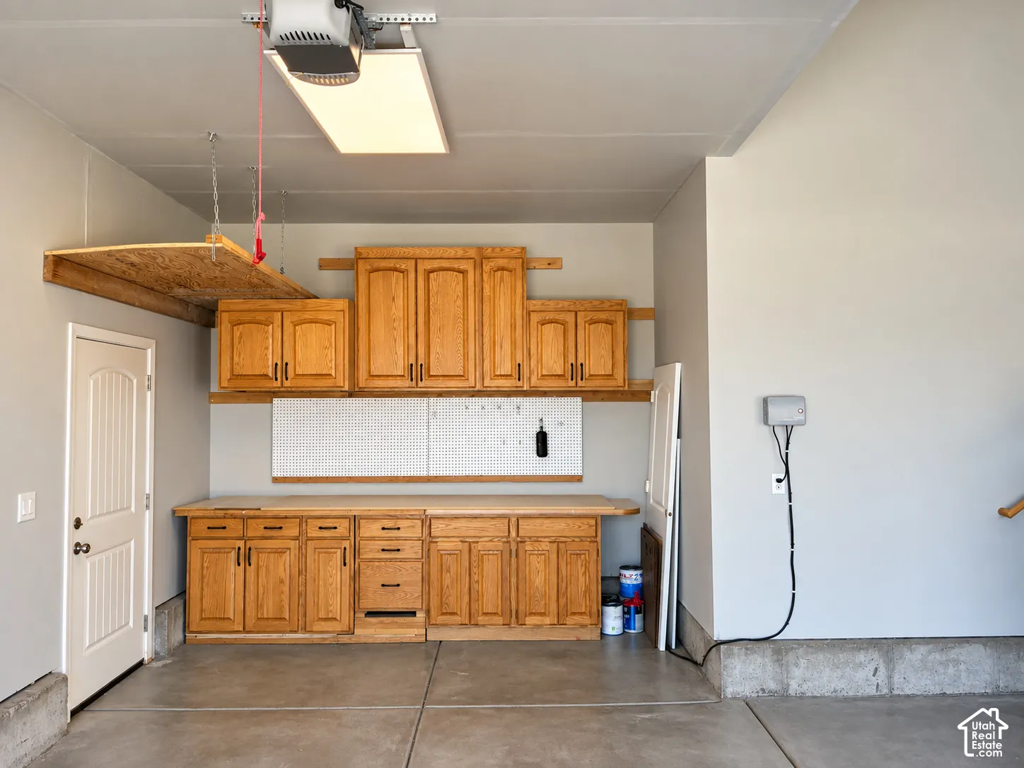 Garage with concrete flooring, built-in wooden cabinetry, a wood-finish workbench, and an overhead storage shelf