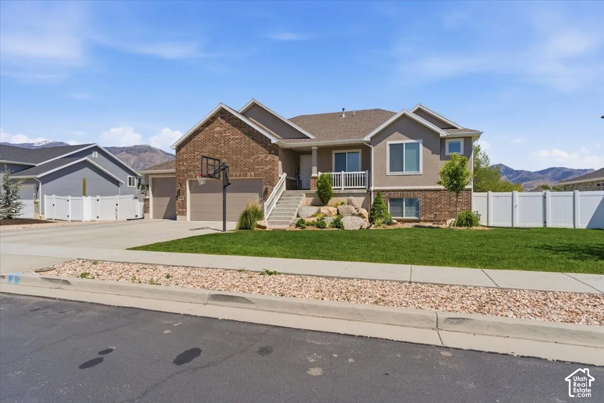 Stucco and brick exterior with a multi-car garage, concrete driveway, and tiered landscaping