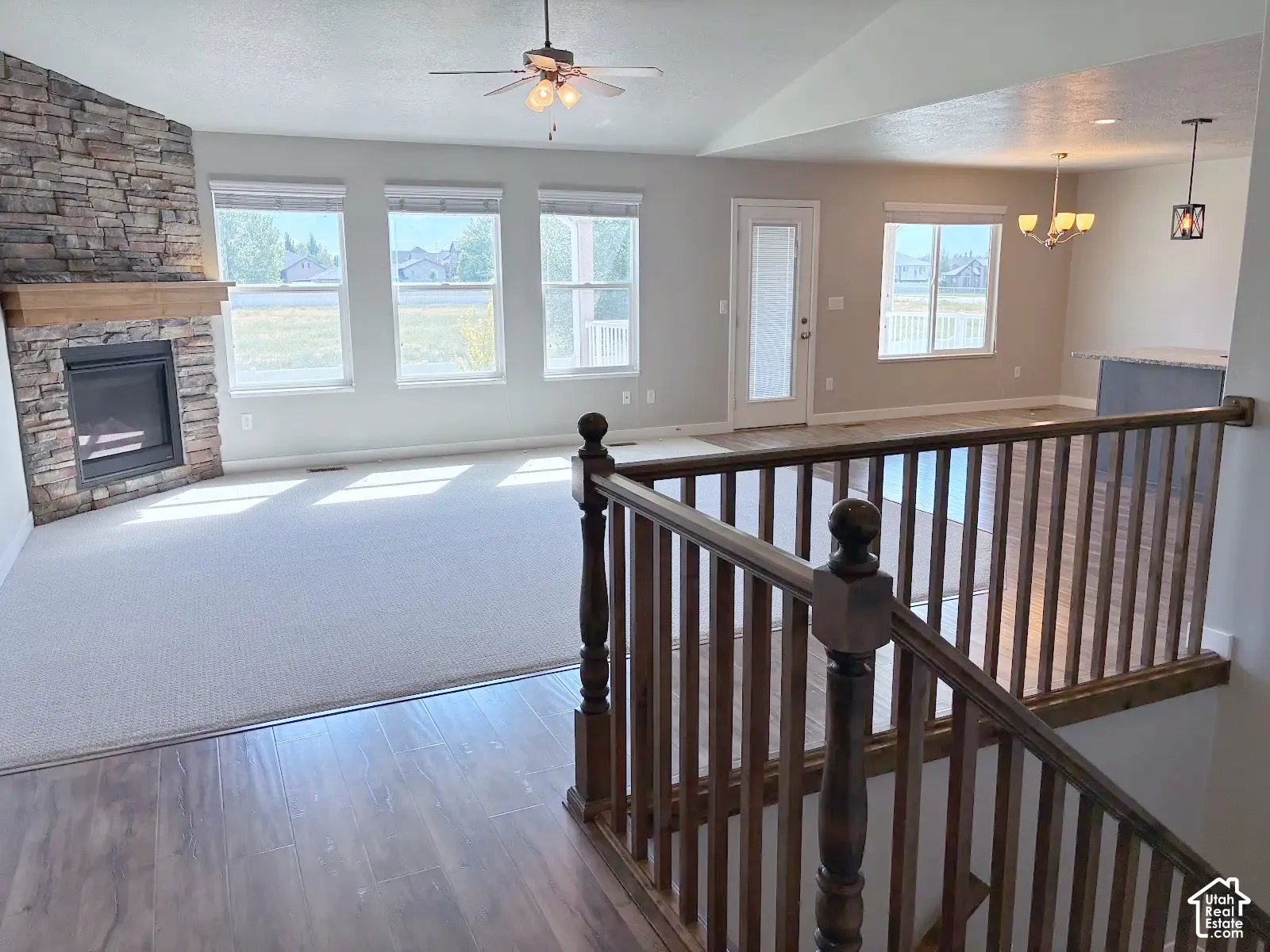 Open-concept living area featuring a stone fireplace with a wood mantle, ceiling fan, and multiple windows