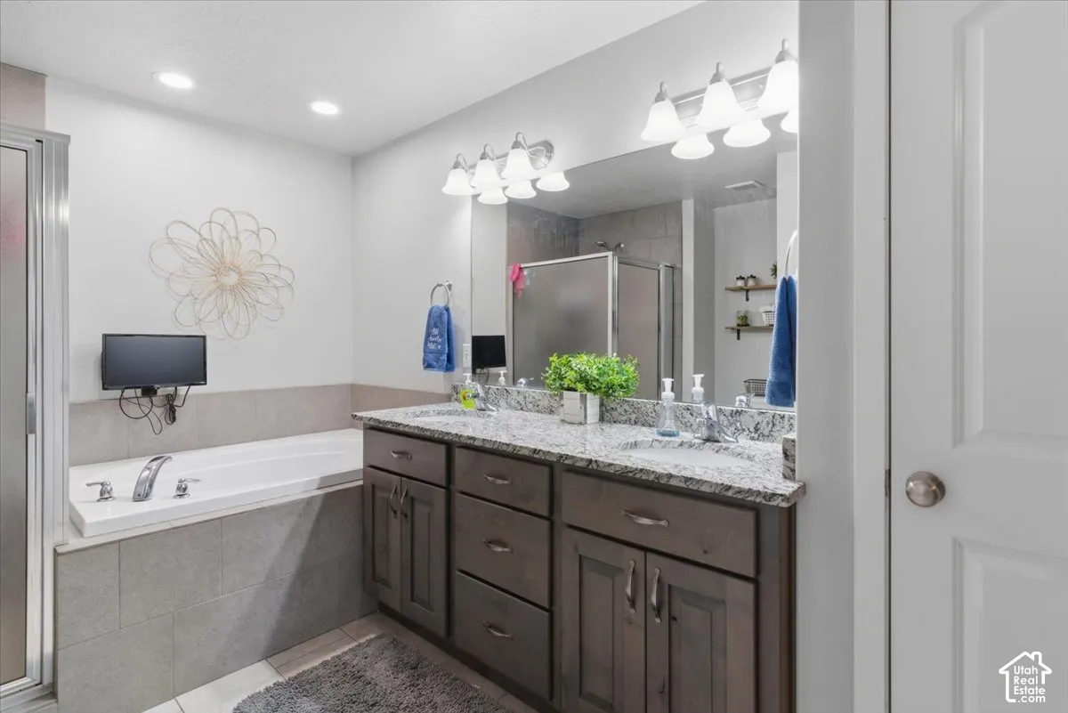 Bathroom featuring a dual-sink vanity with a light-toned countertop, a built-in tub with tile surround, a glass-enclosed shower, and wood-finish cabinetry