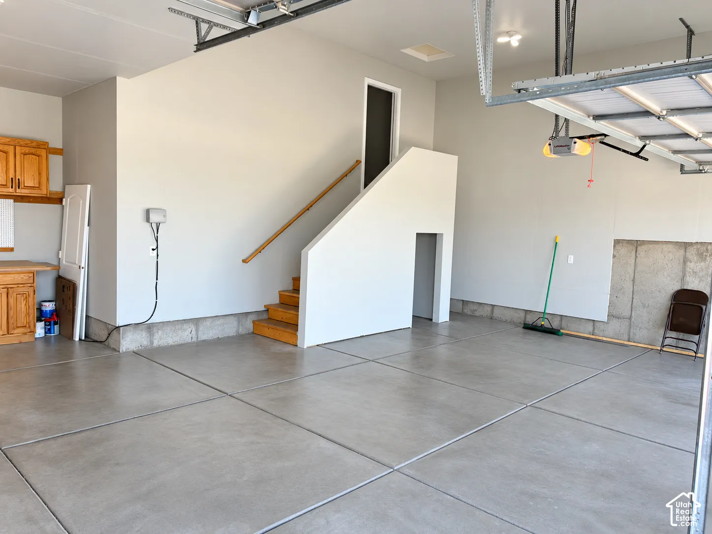 Concrete flooring with expansion joints, built-in wooden cabinetry, stairway with wooden handrail, and an automatic garage door opener
