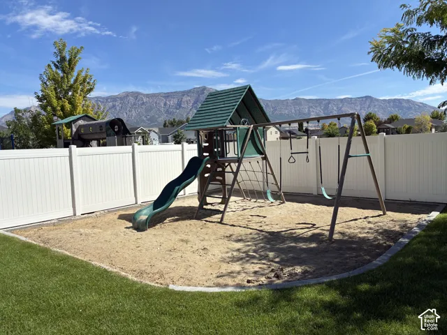 Backyard featuring a play structure, sand area, and a white privacy fence