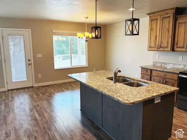 Kitchen featuring a center island with a double basin sink, granite countertops, wood-finish flooring, and pendant lighting