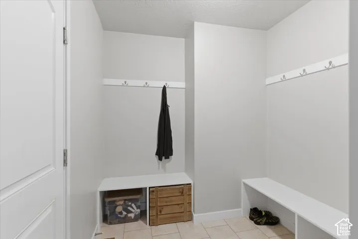 Entryway featuring light neutral wall tones, durable tile flooring, built-in bench seating, and wall-mounted coat hooks