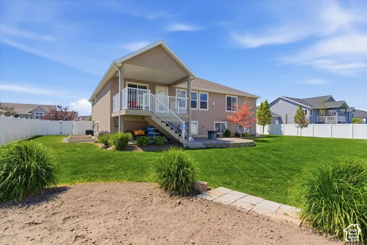 Expansive green lawn with a two-story residence featuring a covered balcony with white railings, and a lower-level patio area