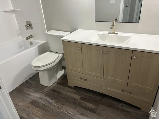 Wood-finish flooring, white bathtub with brushed nickel fixtures, contemporary vanity with a white countertop, under-mount sink, and framed mirror