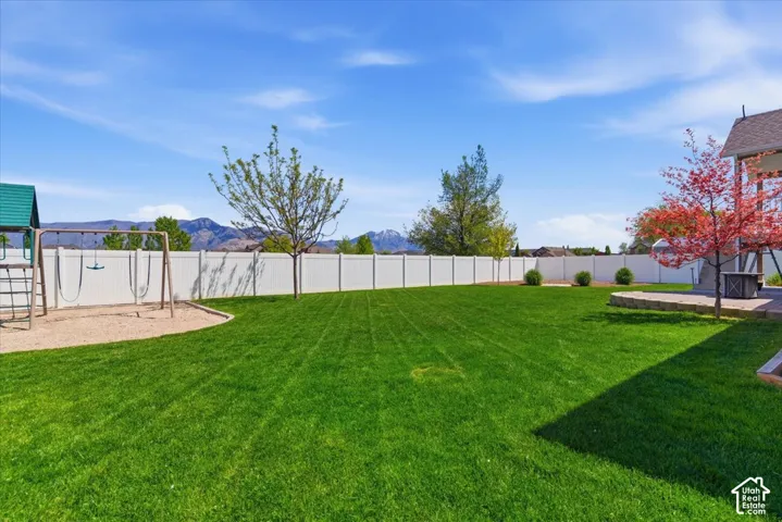 Expansive fenced backyard featuring a substantial lawn, a sand play area, a concrete patio, and mature landscaping