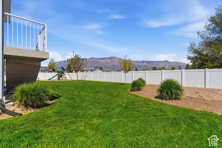 Expansive backyard featuring a manicured lawn, white privacy fencing, and mature trees