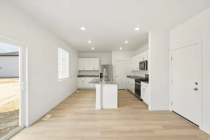 Spacious kitchen featuring an island with granite countertops, white cabinetry, stainless steel appliances, and light wood-finish flooring