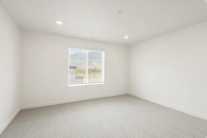 Carpeted room featuring a large window with blinds, recessed lighting, and white baseboards