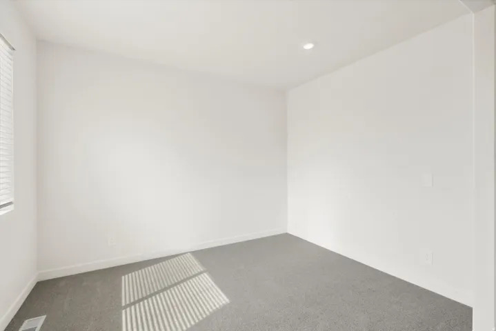 Bright interior space featuring a window with horizontal blinds, neutral wall paint, recessed ceiling lighting, and grey carpeting