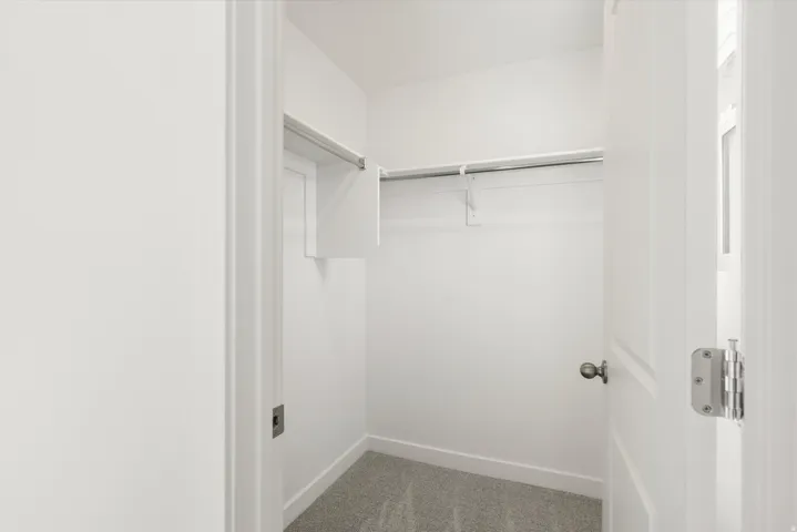 Walk-in closet featuring white walls, grey carpet flooring, and a built-in hanging rod with shelving