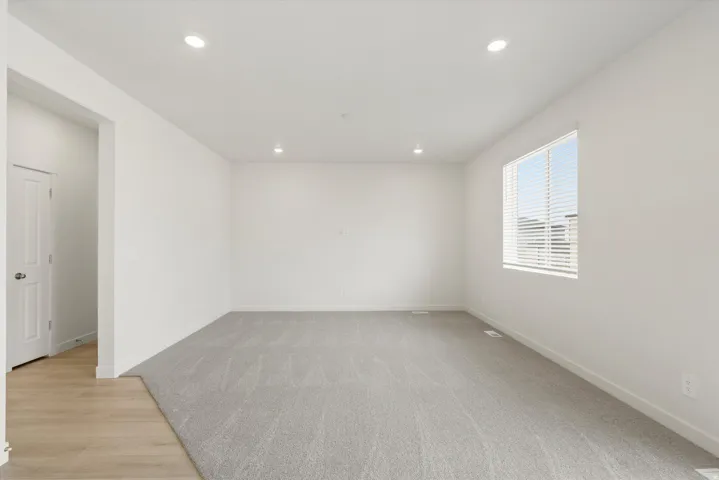 Spacious room featuring light gray carpeting and a large window with white blinds