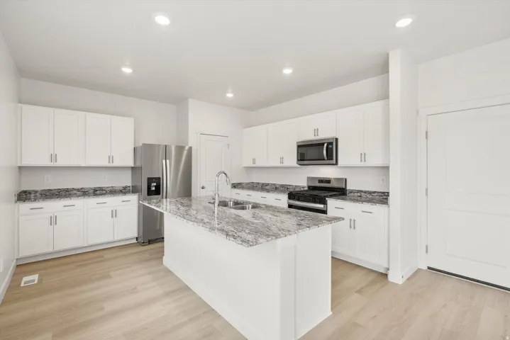 Bright kitchen featuring a central island with a double basin sink, white cabinetry, stainless steel appliances, and light wood-finish flooring