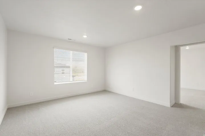 Carpeted interior space featuring a window with blinds, recessed lighting, and a neutral color palette
