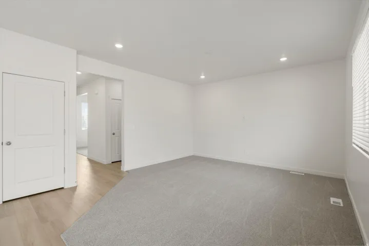 Spacious room featuring light gray carpeting, recessed lighting, white walls, and a window with blinds
