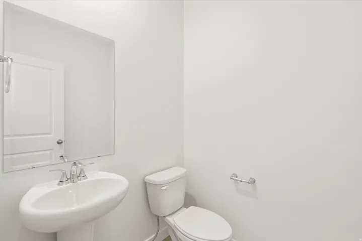 Pedestal sink with chrome faucet, large frameless mirror, and neutral white walls