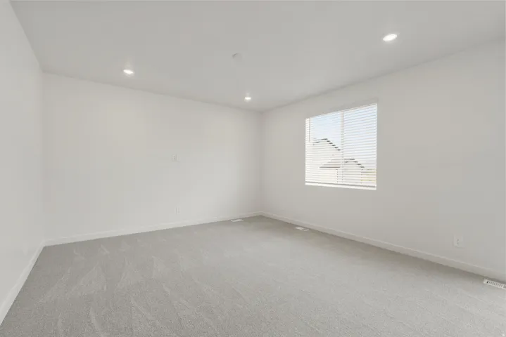 Neutral interior room featuring light gray carpeting, crisp white walls, recessed ceiling lighting, and a window with horizontal blinds