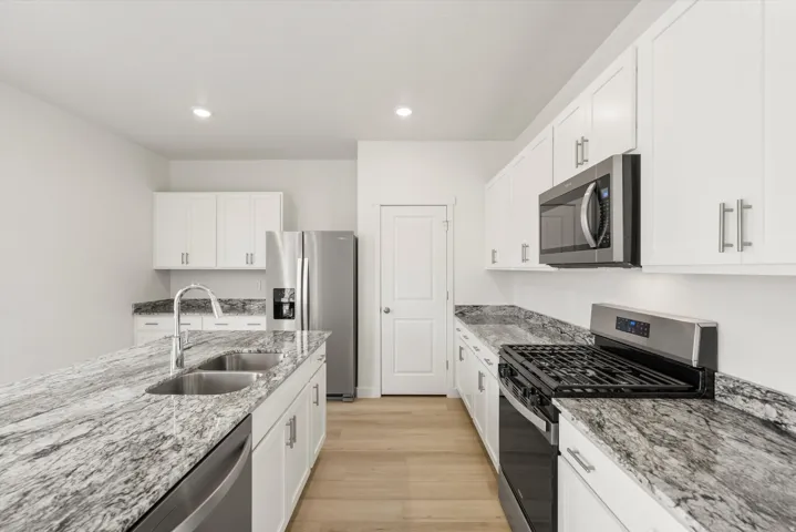 Bright kitchen featuring an island with a double basin sink, stainless steel appliances, granite-look countertops, white cabinetry, and wood-finish flooring