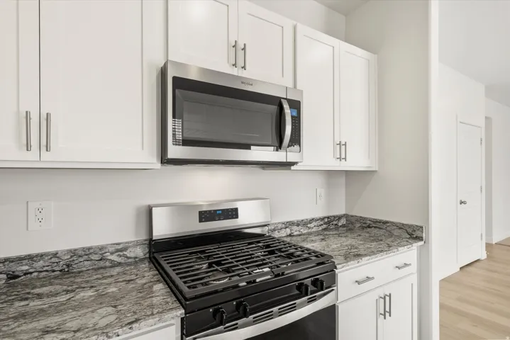 Kitchen featuring a stainless steel range and microwave, white shaker-style cabinetry with brushed nickel hardware, and granite countertops