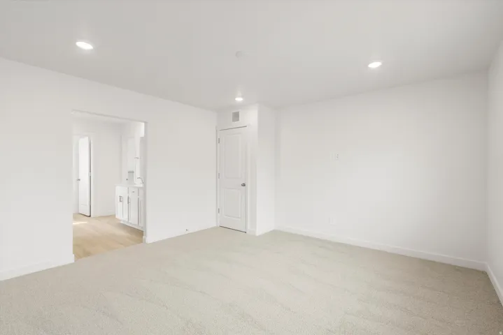 Spacious room featuring neutral carpeting, recessed ceiling lighting, and crisp white walls