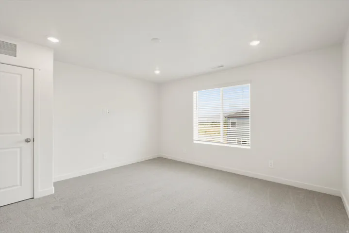 Spacious room featuring neutral carpeting, white walls, recessed ceiling lighting, a window with blinds, and a white interior door