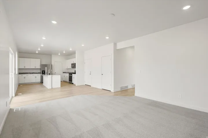 Open-concept living area featuring light-toned wood-finish flooring, recessed lighting, and a modern kitchen with white cabinetry