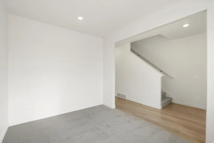 Recessed lighting illuminates the space, featuring a light gray carpeted area and wood-finish flooring