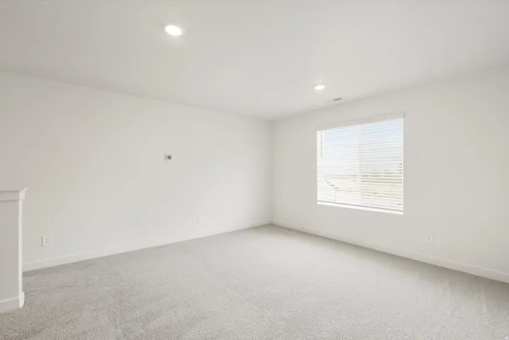 Spacious room featuring light gray carpet flooring, white walls, and a large window with horizontal blinds