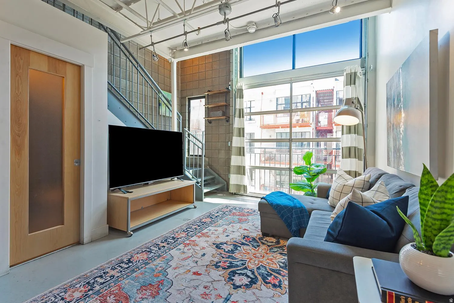Open-concept living area featuring a full-height glass garage door, exposed ceiling beams with track lighting, and a spiral staircase