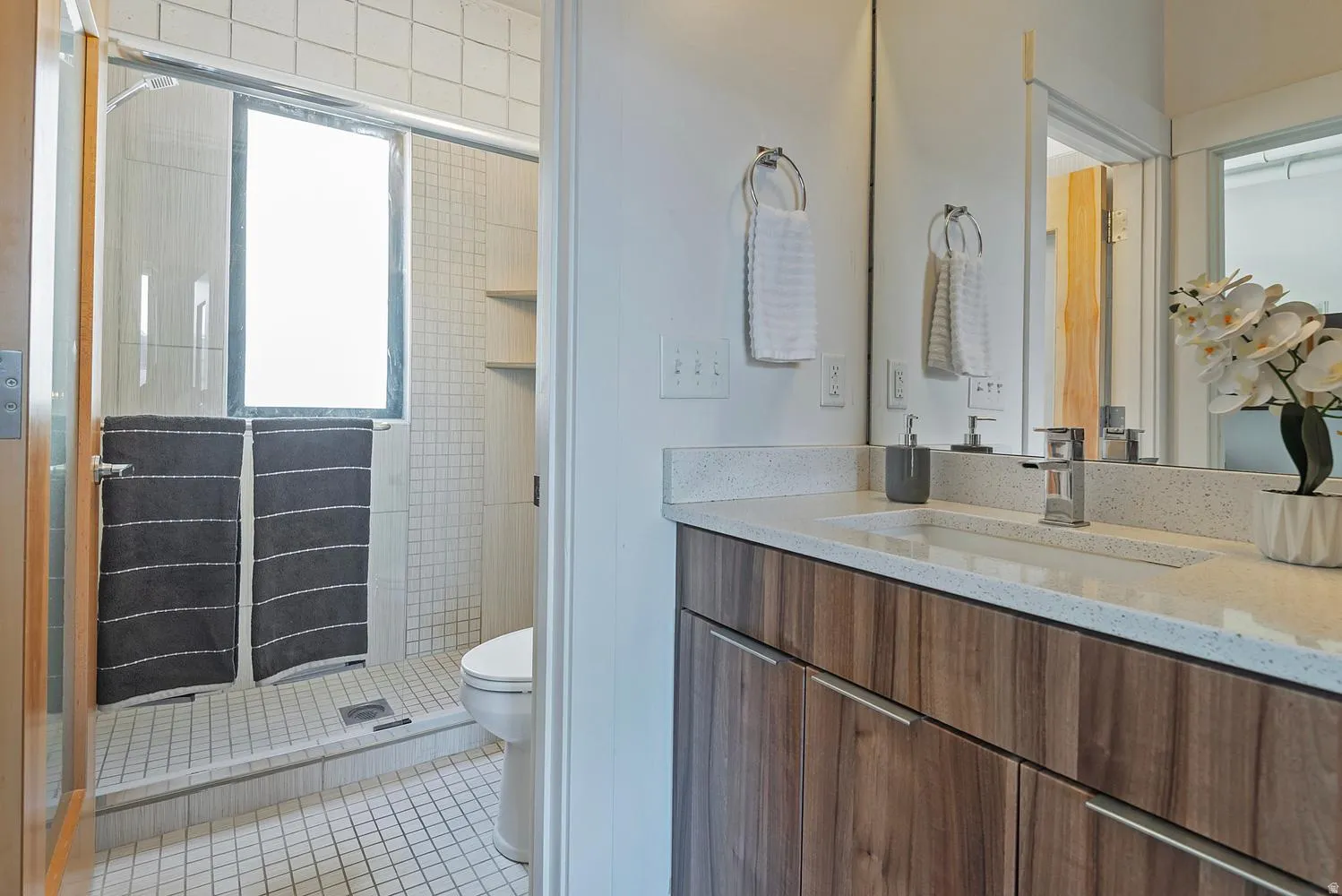 Bathroom vanity featuring a wood-finish cabinet with chrome hardware, an integrated rectangular sink, and a speckled light-toned countertop